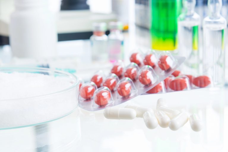 Cartelas de comprimidos vermelhos e azuis e tubos de ensaio em cima de uma mesa branca