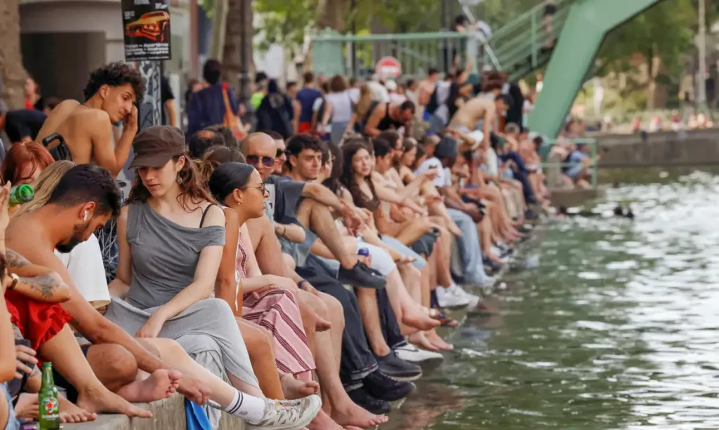 People sit along the Canal Saint-Martin to find some relief from the heat as public swimming having been allowed earlier on part of it due to rising of temperatures, in Paris as a heatwave hits a large of France, June 18, 2026. REUTERS/Alice Sacco