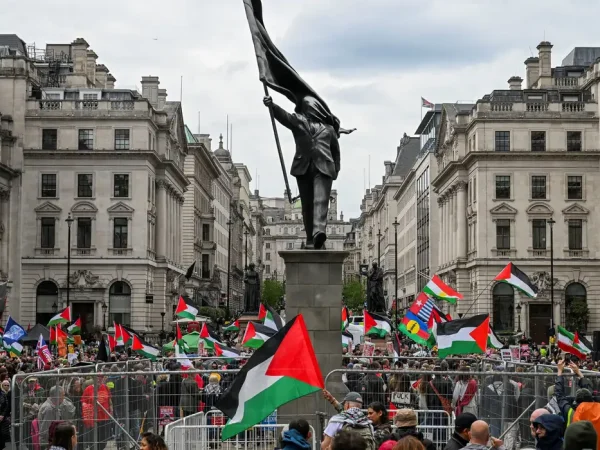 Pessoas seguram bandeiras palestinas ao lado de uma estátua, representando uma figura carregando uma bandeira cobrindo o rosto e descendo de um pedestal, do artista de rua britânico Banksy, durante uma marcha, realizada pela Palestine Solidarity Campaign, para marcar o 78º aniversário da Nakba e contra o comício