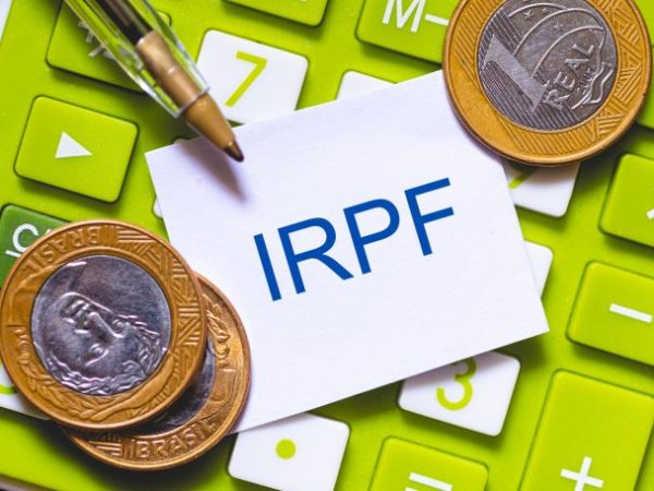 Imagem mostra moedas, uma caneta e um papel com a sigla IRPF (Imposto sobre a Renda da Pessoa Física) em cima de uma calculadora