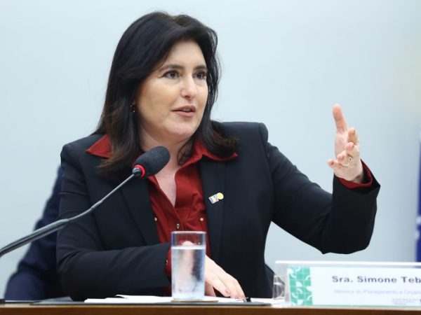 Ministra do Planejamento, Simone Tebet. Ela é uma mulher clara, com cabelos longos, lisos e escuros. Usa um blazer preto e uma camisa vermelha