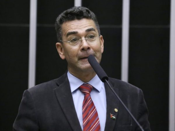 Deputado Padre João fala ao microfone. Ele é claro, tem cabelo escuro, usa óculos, um terno preto, camisa branca e gravata vermelha